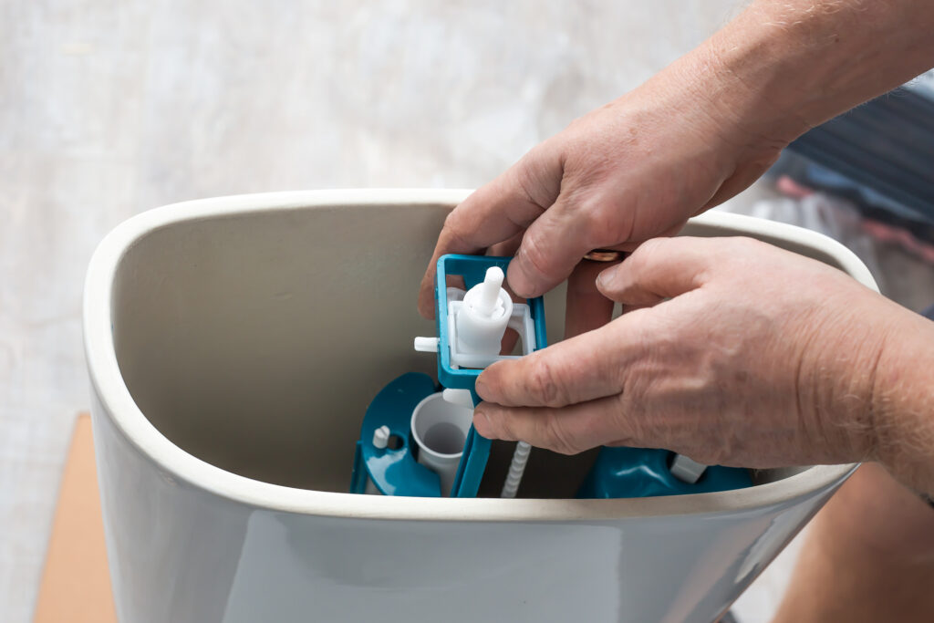 A plumber installs a water pump in a ceramic toilet cistern